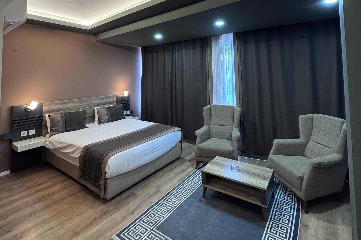 Een moderne hotelkamer met een groot bed, twee fauteuils, een klein tafeltje en een decoratief vloerkleed.