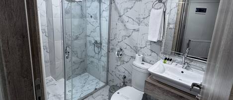 A modern bathroom with a glass-enclosed shower, a white toilet, a sink with a mirror, and marble-patterned walls.