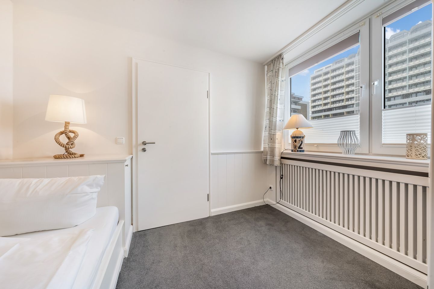 Ein Hotelzimmer mit Bett, Tür, einem Fenster mit Jalousien und einem Heizkörper.