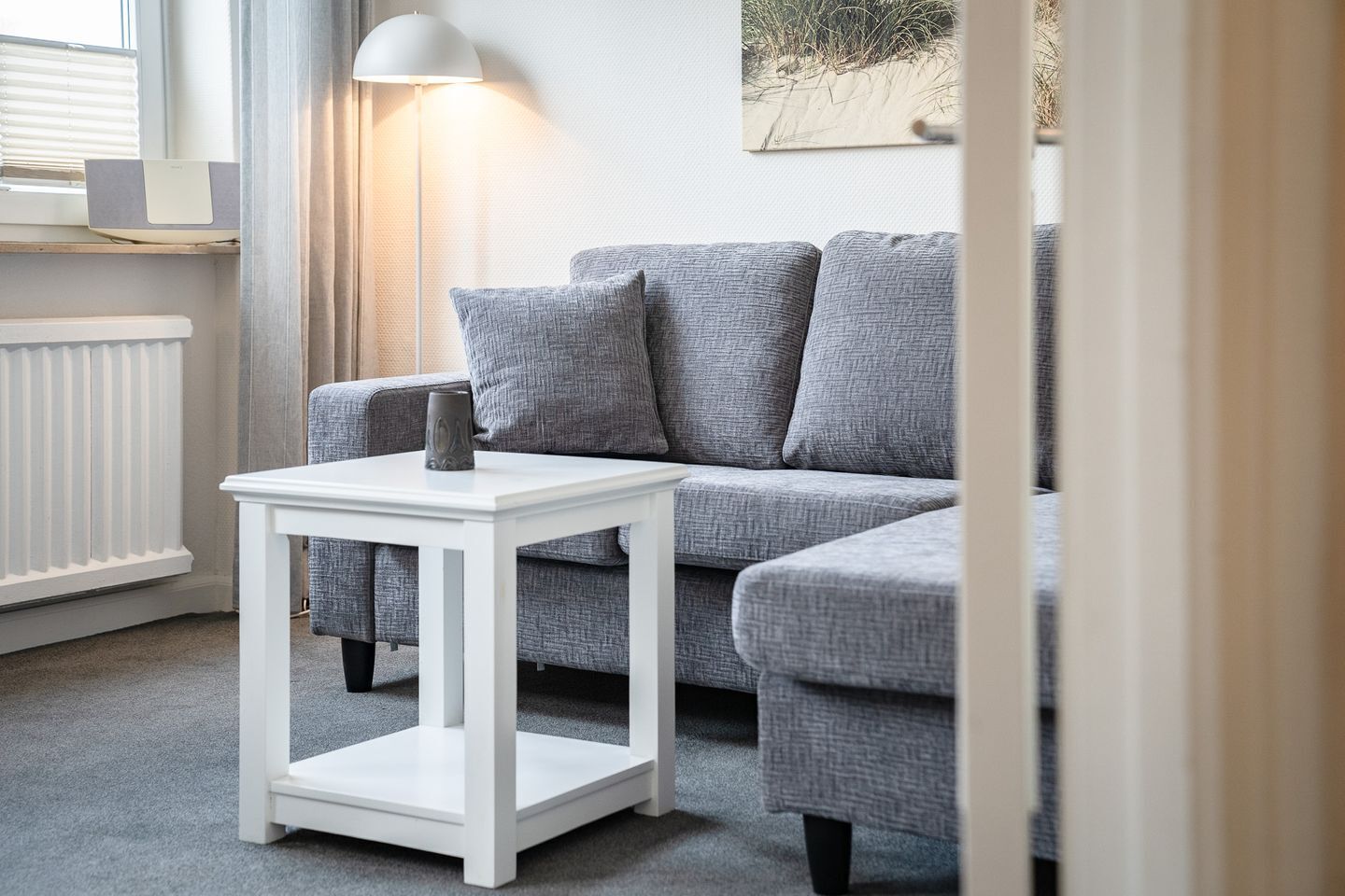 Un canapé gris, une table d’appoint blanche et une lampe.