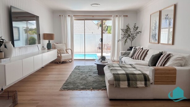 Ett modernt vardagsrum med en soffa, ett soffbord, en tv och utsikt över en pool genom stora fönster.
