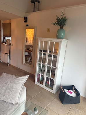 Una sala de estar con una mesa de centro de vidrio, un sofá blanco, un mueble blanco con puertas de vidrio y una pequeña planta en un estante.