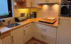 A modern kitchen with a stainless steel sink, a toaster, a kettle, and a wooden cutting board. - Forest cottage by the sea (Sint Maartensvlotbrug)