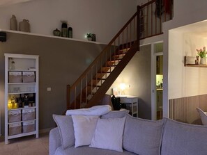 A living room with a staircase, a white storage unit, and a cozy sofa. - Forest cottage by the sea (Sint Maartensvlotbrug)