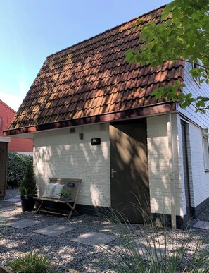 Ein kleines, eingeschossiges Gebäude mit einem geneigten Dach, einer Haustür und einer Bank davor.