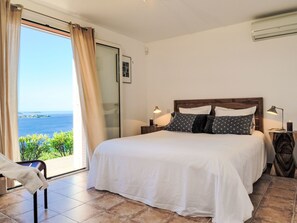 A bedroom with a large bed, a view of the sea, a sliding glass door, and a small table with a lamp. - Vacation home Anto by Interhome (Porto Vecchio)