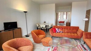 A modern living room with a sofa, armchairs, a coffee table, and a TV. There is a dining area in the background with a table and chairs. - Seasonal rental saint Raphael Valescure 80m² 4 beds (Saint-Raphaël)