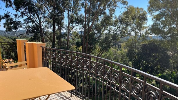 A balcony with a table and chairs, surrounded by a metal railing with a view of trees and hills. - Seasonal rental saint Raphael Valescure 80m² 4 beds (Saint-Raphaël)