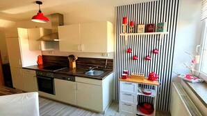 Une cuisine moderne avec des meubles blancs, un plan de travail noir et un luminaire suspendu rouge.