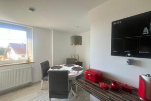 A dining area with a round table, chairs, a red suitcase, a kettle, and a wall-mounted notes board. - Hochsitz Appartement (Seelitz)