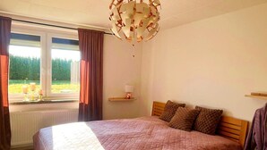 Une chambre avec un grand lit, une fenêtre avec des rideaux, un lustre et une vue sur la verdure.