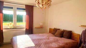 Ein Schlafzimmer mit einem großen Bett, einem Fenster mit Vorhängen, einer Chandelier und Blick ins Grüne.