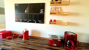 Une cuisine avec un calendrier noir, des appareils électroménagers rouges et des étagères en bois où sont posés des livres et des tasses.