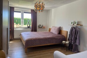A bedroom with a bed, a bedside table, a lamp, a hanging robe rack, and a window with curtains.