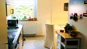 Une cuisine compacte dotée d’une fenêtre, d’un évier, d’un four à micro-ondes et d’un petit coin repas avec une chaise et une table.