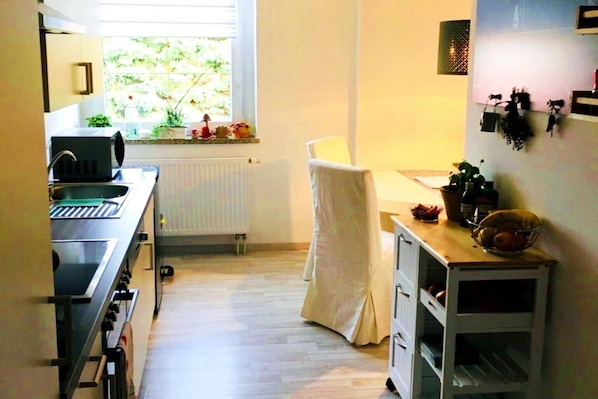 A compact kitchen with a window, a sink, a microwave, and a small dining area with a chair and a table.