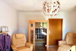 A room with two beige armchairs, a wooden door, a glass door leading outside, and a ceiling light fixture.