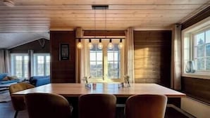 Un intérieur en bois avec une table à manger, des chaises et de grandes fenêtres.