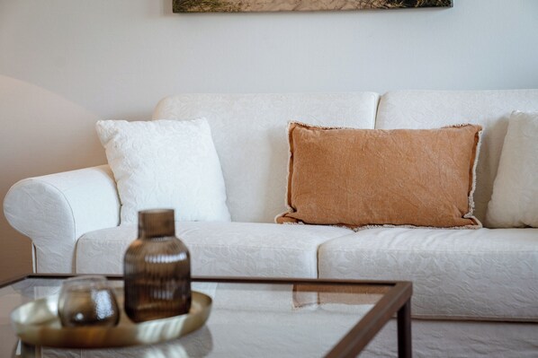 A white sofa with a textured fabric and two pillows, one white and one brown. - 62 m² 2-room vacation apartment in Kampen with a view of the sea, for up to 3 people (Kampen (Sylt))