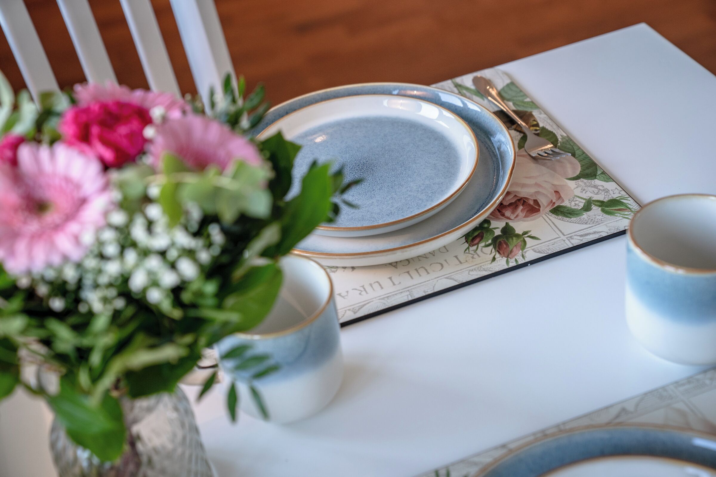 Ett dukat bord med tallrikar, en vas med blommor och en meny.