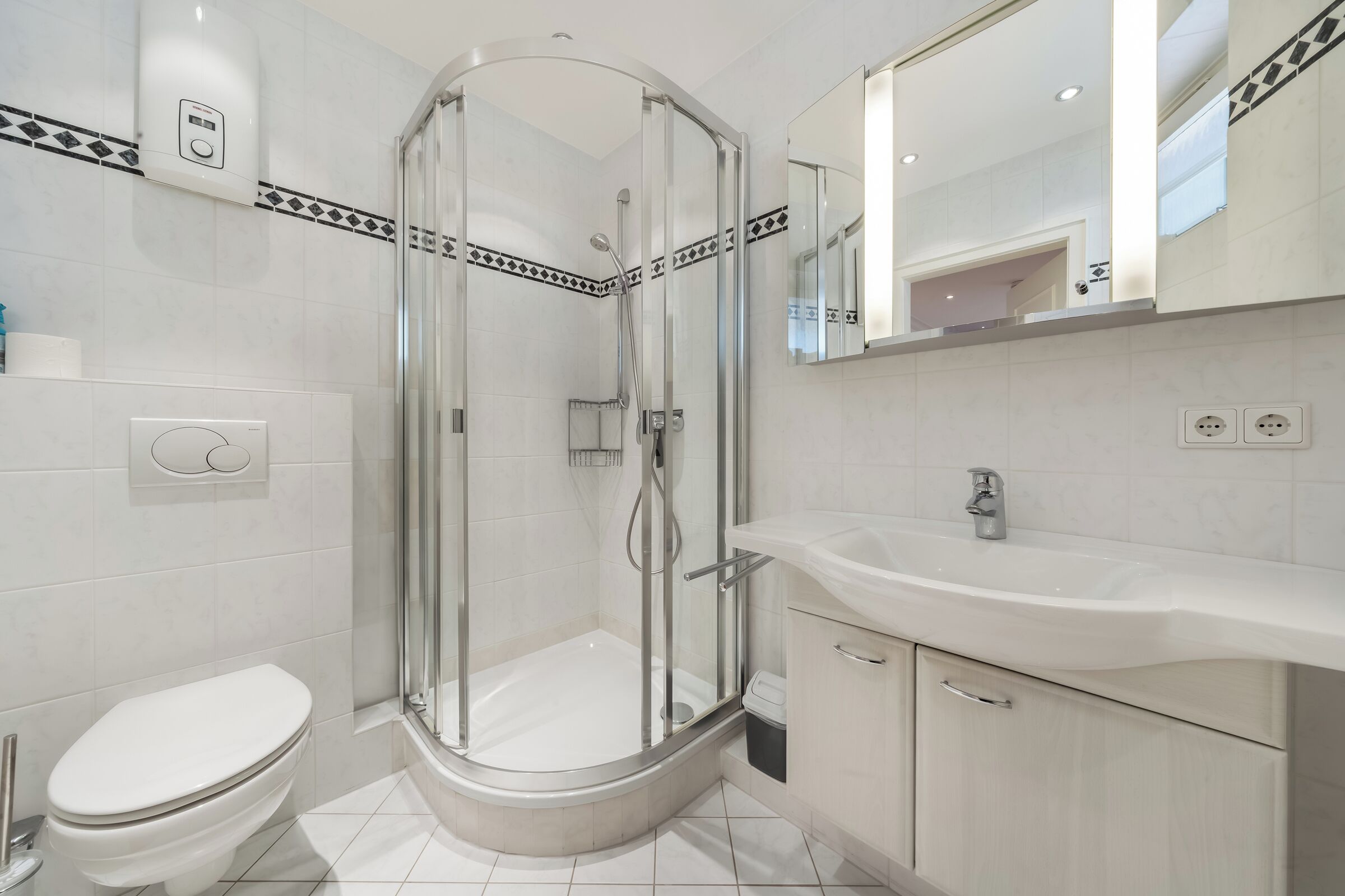 Un baño moderno con ducha de vidrio, inodoro blanco y lavamanos con espejo.