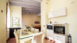 Una cucina compatta con zona pranzo, che include un tavolo con piano in vetro, sedie bianche e un forno integrato.