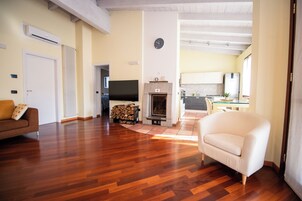 Un soggiorno spazioso con pavimento in parquet, un camino, una televisione e una cucina sullo sfondo.