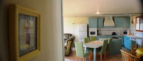 Un área de comedor con una mesa y sillas, una cocina con gabinetes y electrodomésticos, y un cuadro en la pared.