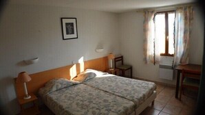 Quarto de hotel com cama de casal, mesas de cabeceira, escrivaninha e janela com cortinas.