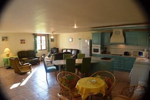 A dining area with a table and chairs, a kitchen with blue cabinets, and a living area with a sofa and a lamp. - Villa La Treille 1 avec piscine près des gorges de l’Ardèche (Grospierres)