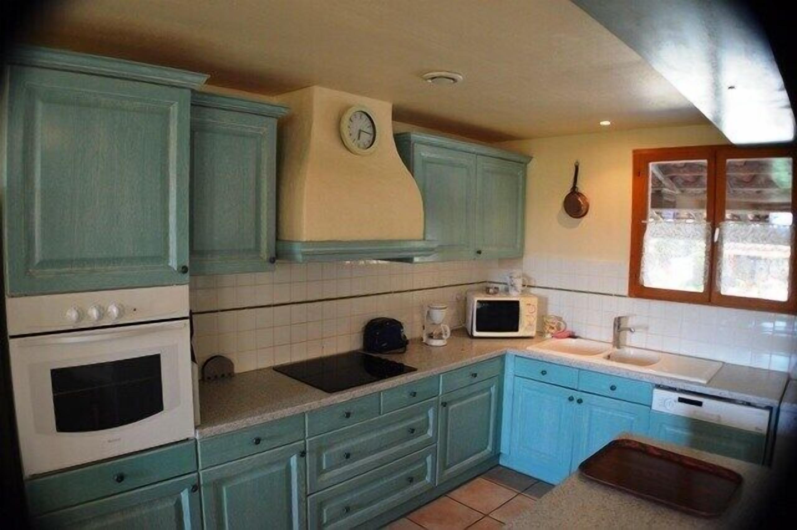 A kitchen with teal cabinetry, a microwave, a sink, and a clock on the wall.