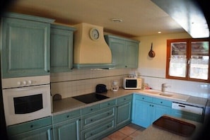 A kitchen with teal cabinetry, a microwave, a sink, and a clock on the wall. - Villa La Treille 1 avec piscine près des gorges de l’Ardèche (Grospierres)