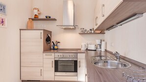 A compact kitchen with a built-in oven, a sink, and wooden cabinets. - Apartment Kleine Auszeit 02 - cozy domicile in the center of Koserow (Koserow)