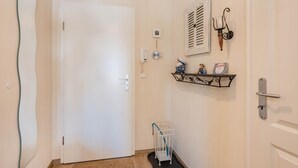 A hallway with a white door, a small shelf with decorative items, a baby crib, and a wall-mounted phone. - Apartment Kleine Auszeit 02 - cozy domicile in the center of Koserow (Koserow)