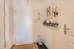 A hallway with a white door, a small shelf with decorative items, a baby crib, and a wall-mounted phone. - Apartment Kleine Auszeit 02 - cozy domicile in the center of Koserow (Koserow)