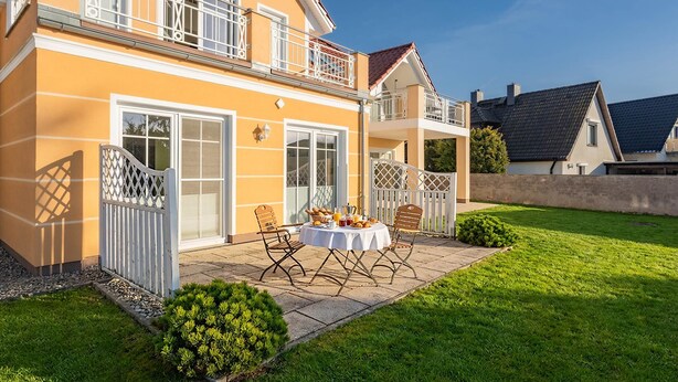 A two-story house with a balcony, a patio with a table and chairs, and a well-maintained lawn. - Apartment Kleine Auszeit 02 - cozy domicile in the center of Koserow (Koserow)