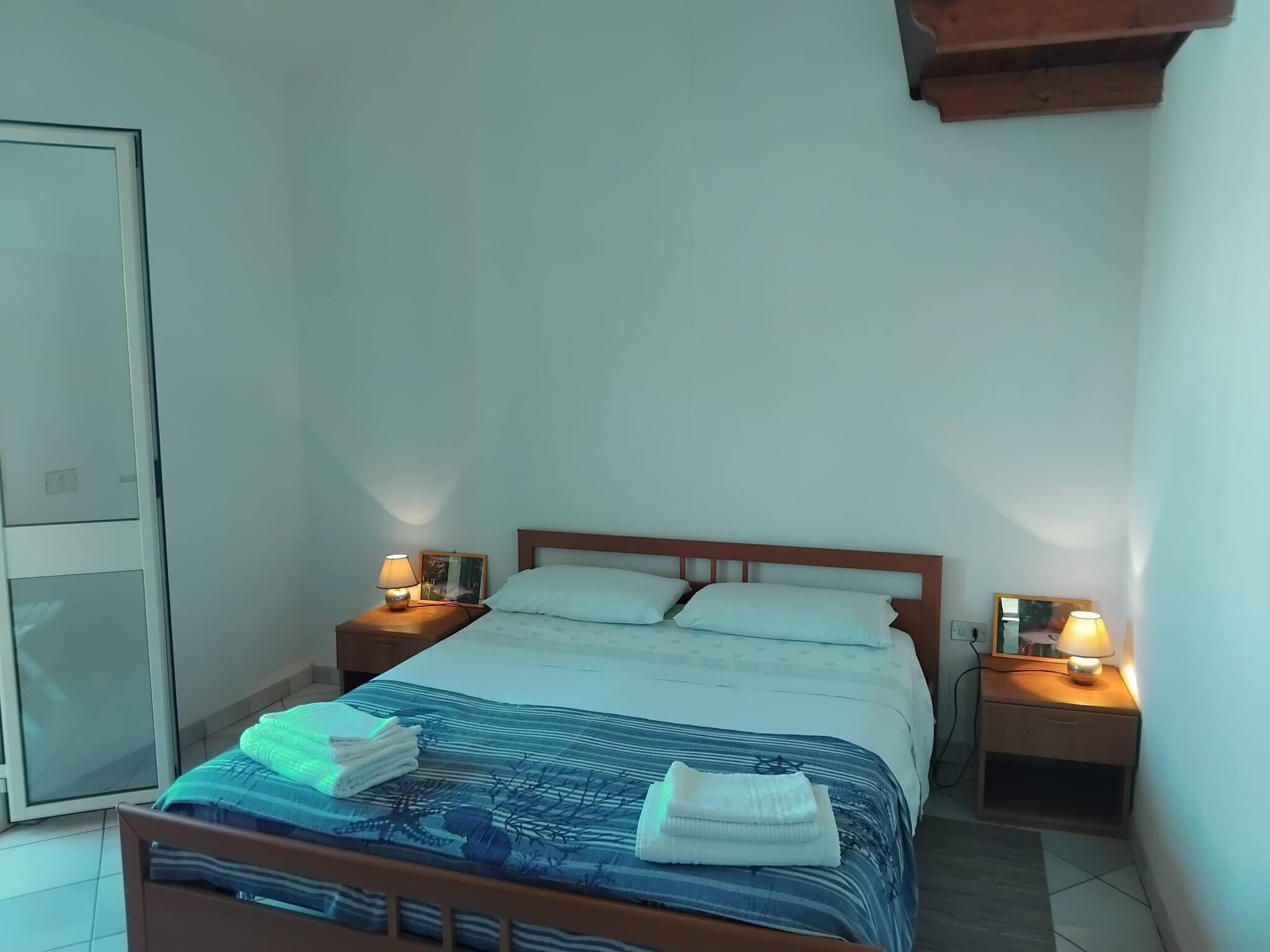 A neatly made bed with a blue and white striped bedspread, two pillows, and folded towels on the side. There are two bedside lamps on wooden nightstands.