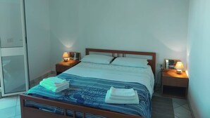 A neatly made bed with a blue and white striped bedspread, two pillows, and folded towels on the side. There are two bedside lamps on wooden nightstands. - Is Araus Holiday apartment for 4 people 50 meters from the sea in Mandriola (Mandriola)