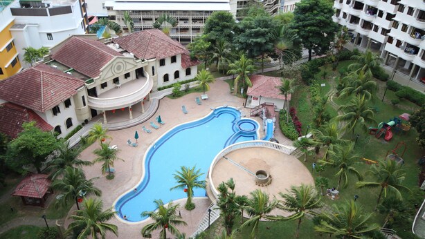 A resort with a swimming pool, palm trees, and a building with a red-tiled roof. - Seaview Condo with Pool (Batu Ferringhi)