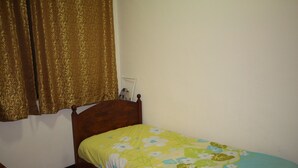A small, single-bed room with a wooden headboard, a floral bedspread, and a curtain on the window. - Seaview Condo with Pool (Batu Ferringhi)