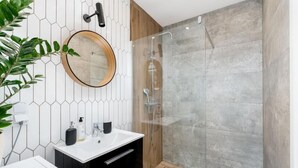 A modern bathroom with a white sink, black cabinets, a round mirror, and a glass shower enclosure. - Malila Apartments Konopnickiej 63E (Kraków)