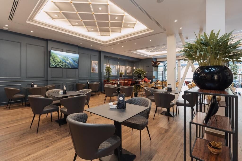 A modern restaurant with a high ceiling, recessed lighting, and a variety of seating arrangements including tables and chairs.