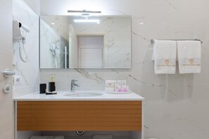A modern bathroom with a marble backsplash, a white sink, a mirror, a hairdryer, and two towels hanging on a rack. - Hotel Boutique Vila 135 (Tirana)