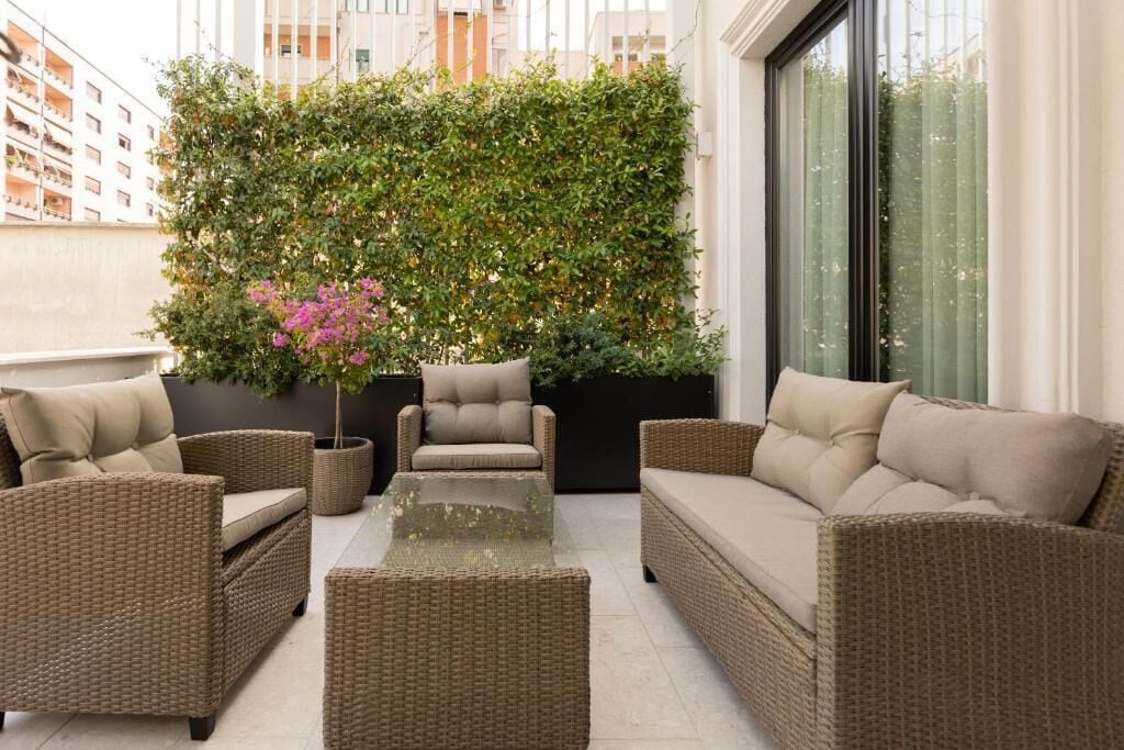 A balcony with wicker furniture, a glass-top table, and a large green wall with plants and flowers.