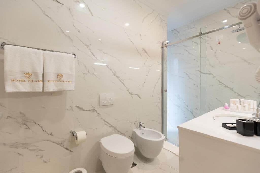 A modern bathroom with marble walls, a toilet, bidet, and a shower area.