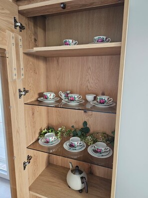 A wooden cabinet with three shelves, each holding teacups and saucers. - 53° North Vacation Home - New Construction 2026 (Hinte)