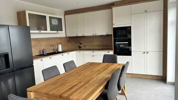Een moderne keuken met een houten eettafel, grijze stoelen, witte kasten en inbouwapparatuur.