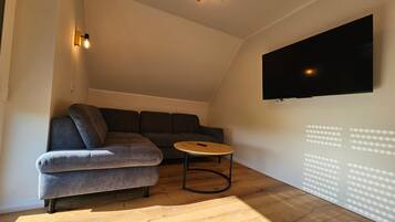 Een moderne woonkamer met een hoekbank, een ronde salontafel en een flatscreen televisie aan de muur.