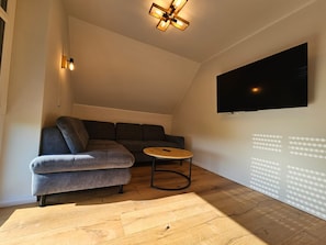 A modern living room with a sectional sofa, a round coffee table, and a flat-screen TV mounted on the wall.