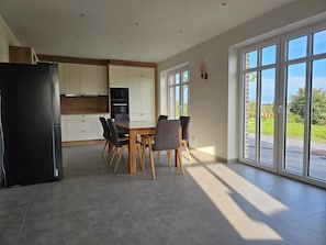 A modern kitchen with a dining area, large windows, and a view of the outdoors.